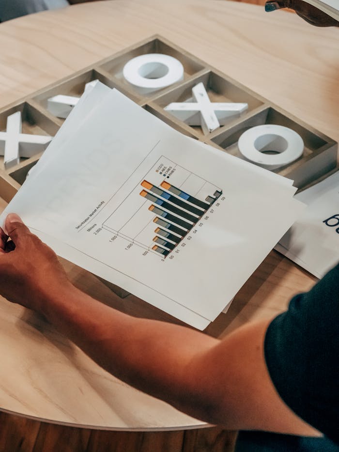 Close-up of hand holding business analysis document with graphs, set on a wooden table indoors.